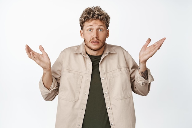 Free Photo confused young blond man shrugging shoulders and raise hands up dont know being clueless have nothing to say standing over white background