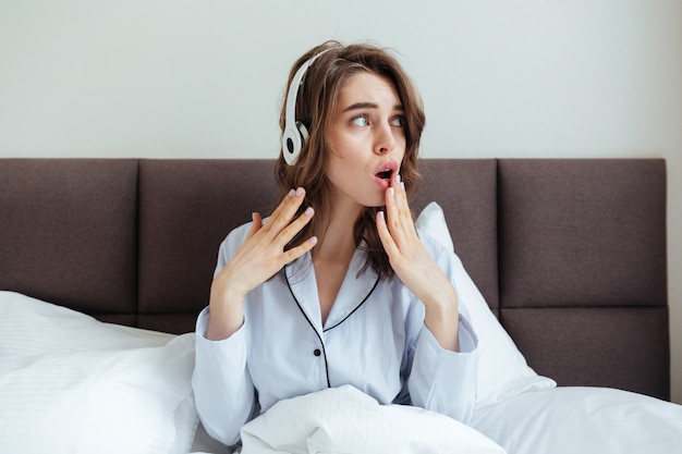 Confused young lady dressed in pajama listening music.