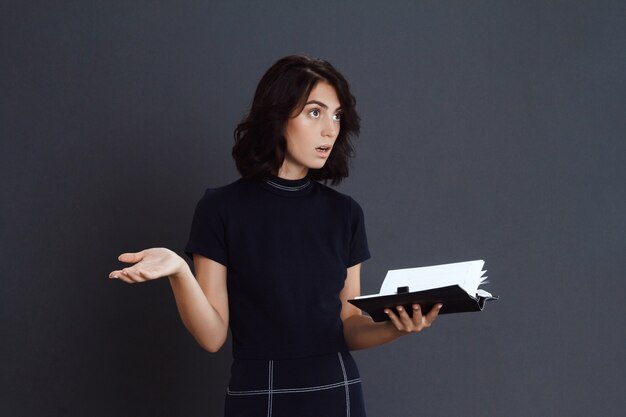 Confused young woman holding notebook in hands