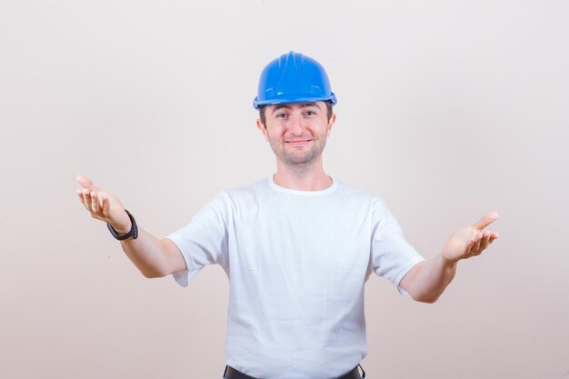 Construction worker opening arms for hug in t-shirt, helmet and looking gentle