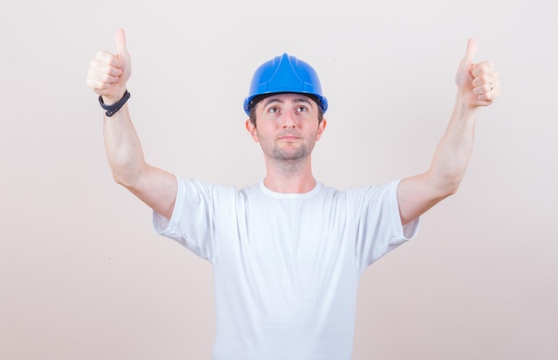 Construction worker showing double thumbs up in t-shirt, helmet and looking confident