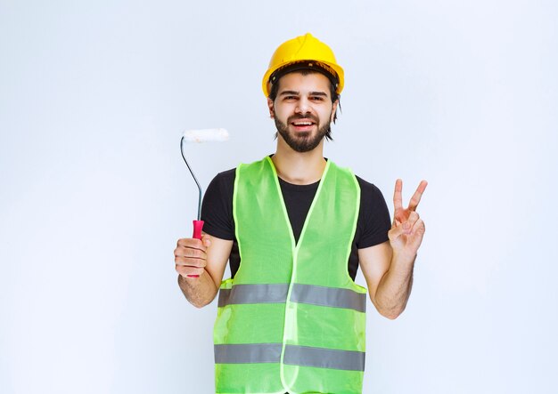 Free photo construction worker with a yellow helmet holding a white trim roller.