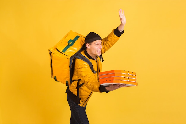 Free photo contacless delivery service during quarantine. man delivers food and shopping bags during insulation. emotions of deliveryman isolated on yellow