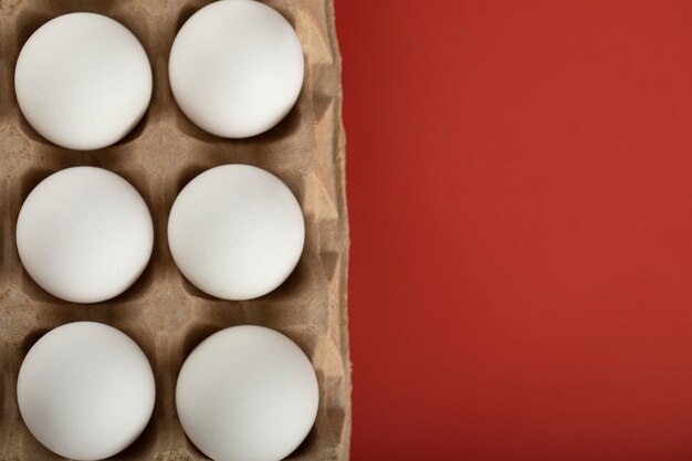 Container of white eggs on red surface. 