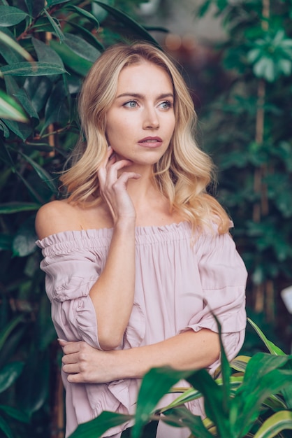 Free photo contemplated blonde young woman standing near the green plants