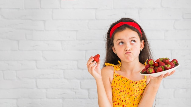 Contemplated girl holding plate of red strawberries