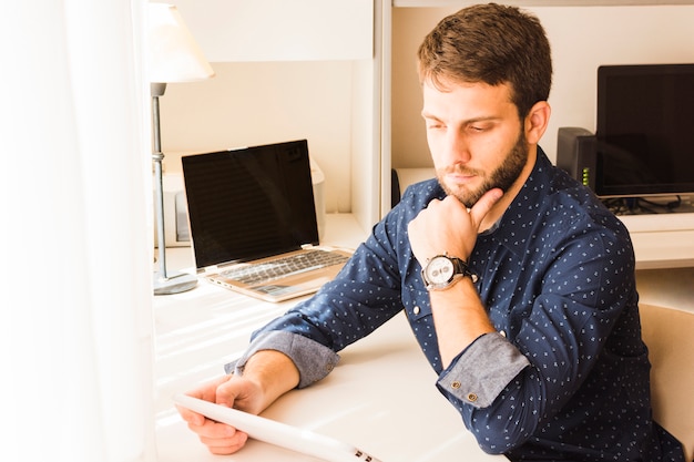 Free photo contemplated handsome young man looking at digital tablet