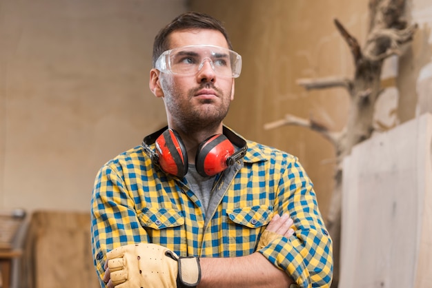 Free photo contemplated male carpenter wearing safety glasses standing with her arms crossed