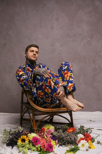 Contemplated young man sitting on chair with colorful flowers thrown on floor