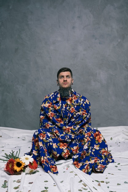 Free photo contemplated young man sitting on floor with crossed legs near the gerbera flowers