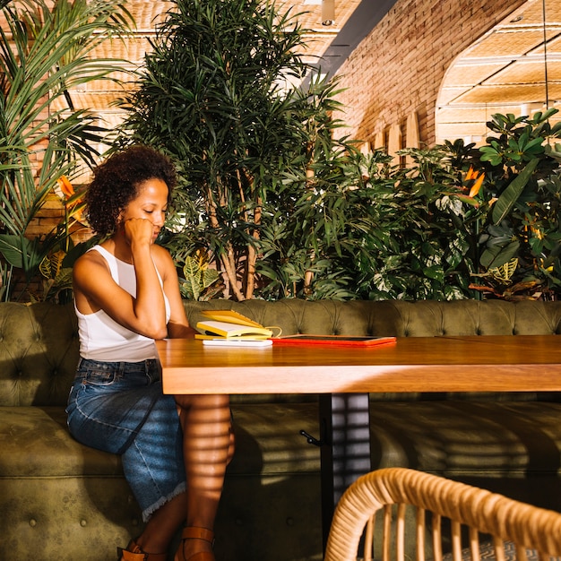 Free Photo contemplated young woman sitting at restaurant table with digital tablet; cellphone and diary