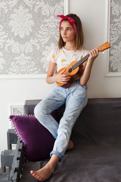 Free photo contemplating girl holding ukulele looking away at home