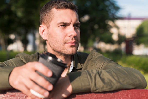 Contemplating man holding disposable coffee cup in park