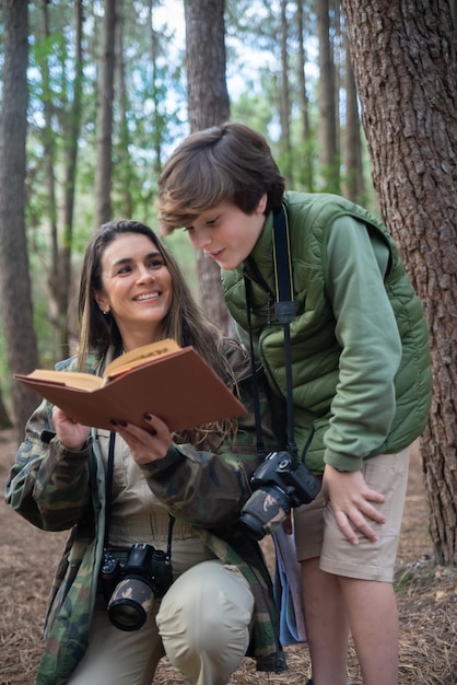 Free photo content family with cameras walking in forest. dark-haired mother and son in coats getting ready to take pictures, discussing route, checking notes. parenting, family, leisure concept