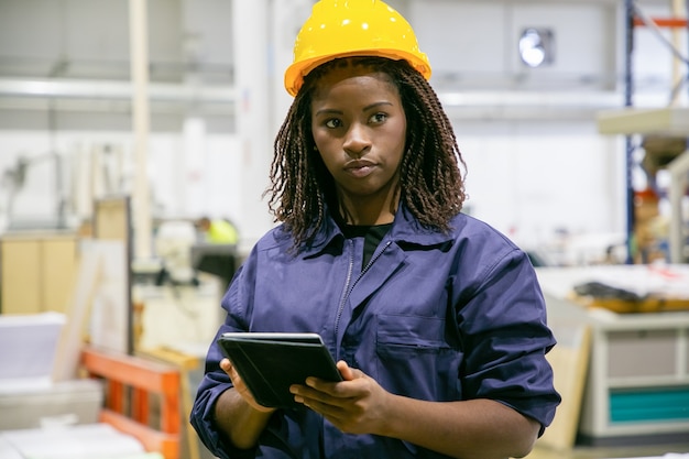 Content female plant worker standing with tablet and looking away