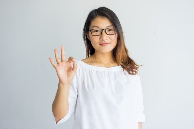 Content pretty Asian girl with highlighted hair making ok sign as symbol of approval.