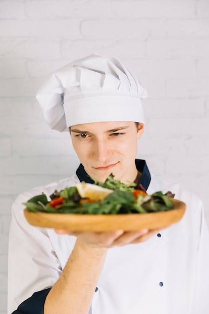 Free photo cook looking at wooden plate with salad