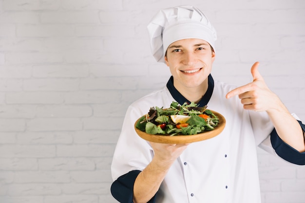 Cook pointing finger at salad on wooden plate 