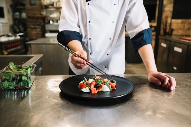 Free photo cook putting green on plate with salad