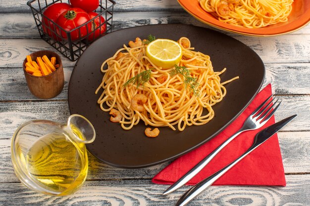 cooked italian pasta with shrimps greens and lemon inside brown plate on grey