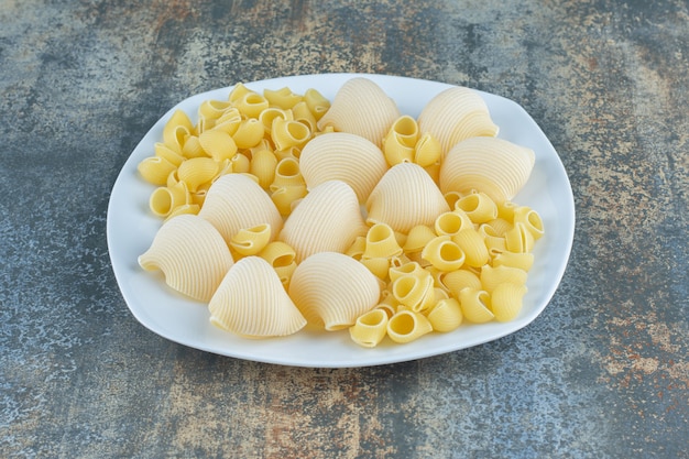 Cooked and uncooked pastas in the bowl, on the marble surface. 