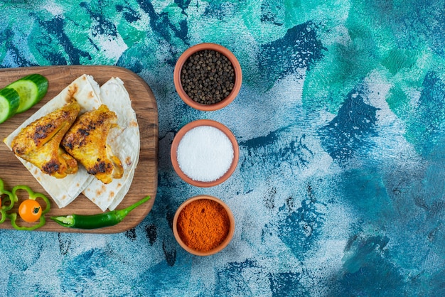 Free photo cooked wings, lavash and vegetables on a cutting board, on the blue background.