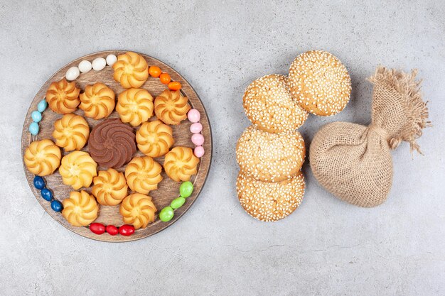 Cookies and candies on wooden board next to cookies and a sack on marble background. High quality photo