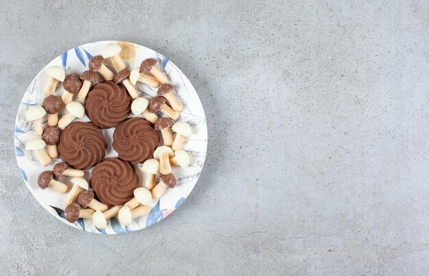 Cookies surrounded by chocolate mushrooms on a plate on marble background.