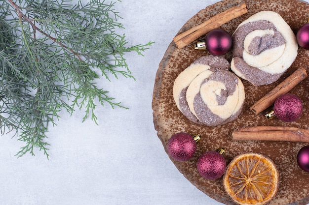 Cookies with baubles, cinnamons and orange slices on wood piece.