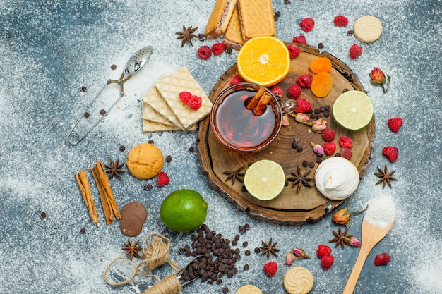 Free photo cookies with flour, tea, fruits, spices, choco, strainer on wooden board and stucco background, top view.