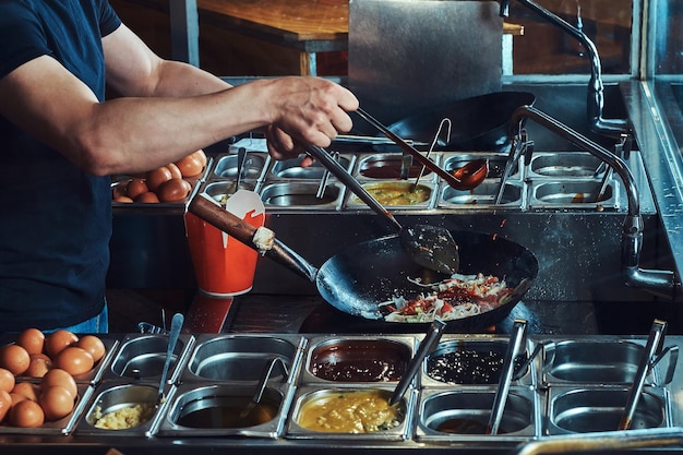 Cooking process in an Asian restaurant. Cook is fry vegetables with spices and sauce in a wok