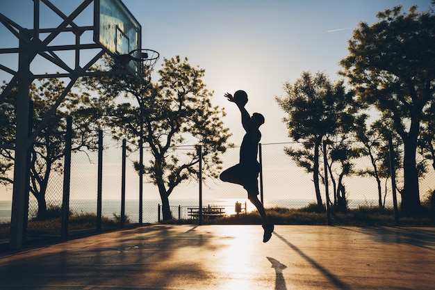 Cool black man doing sports, playing basketball on sunrise, jumping silhouette