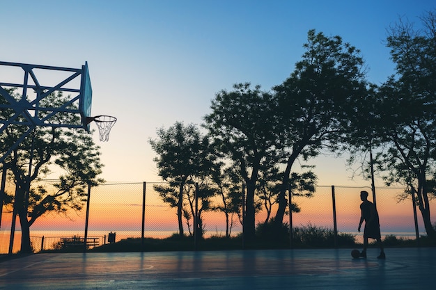 Cool black man doing sports, playing basketball on sunrise, silhouette