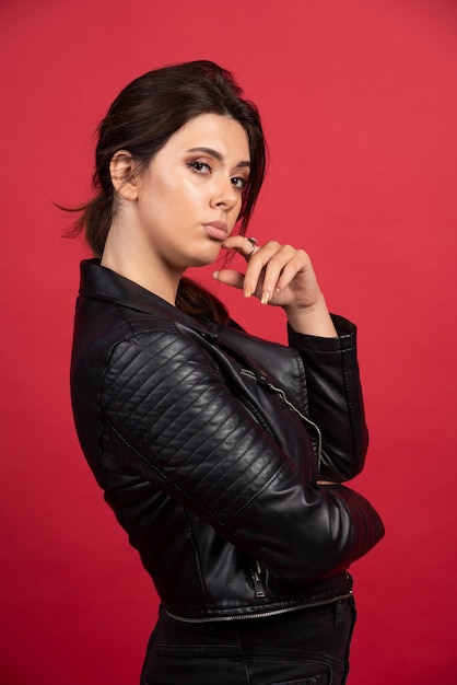 Cool girl in black leather jacket puts her finger to her chin and thinking. 