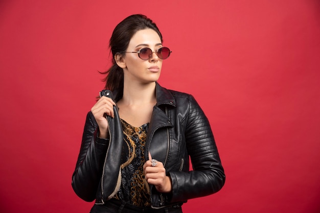 Cool girl in black leather jacket and sunglasses looks strict and demanding. 