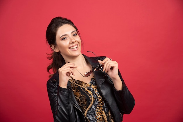 Cool girl in black leather jacket taking out her sunglasses and smiling. 