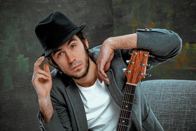 Free Photo cool guy sitting with guitar on gray space