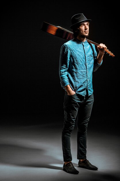 Cool guy standing with guitar on dark wall