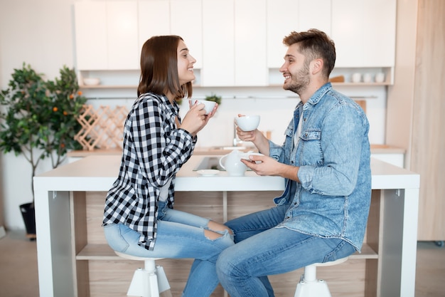 Cool hipster young happy man and woman in kitchen, breakfast, couple together in morning, smiling, having tea