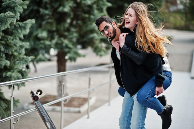 Cool multiracial couple posing with longboard European girl jumped over shoulder arabian man