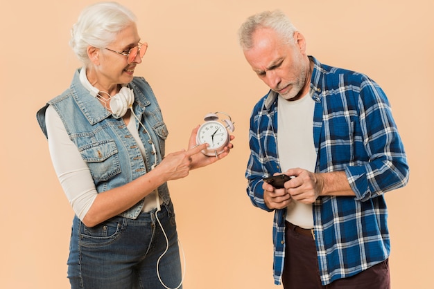 Free Photo cool senior couple with alarm clock and smartphone