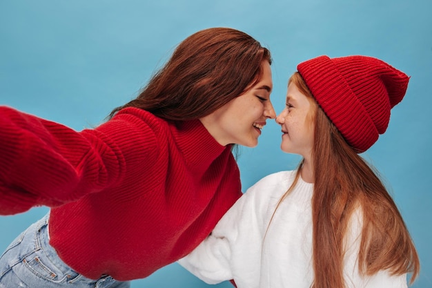 Free Photo cool trendy two sisters in red outfit looking at each other and makes photo on isolated background smiling girls with long hair posing