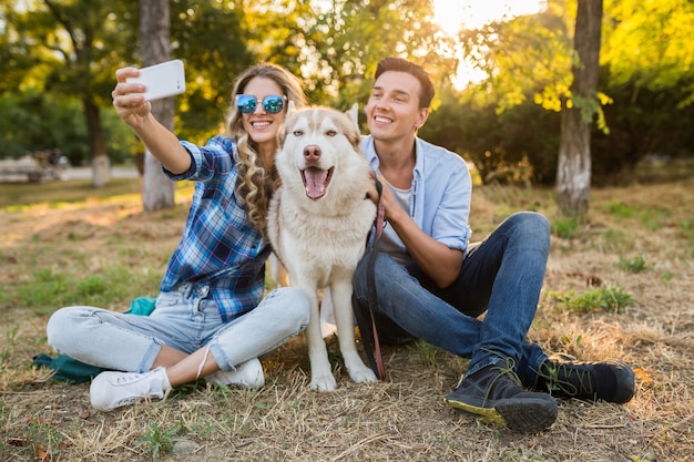 Cool young stylish couple playing with dog in park