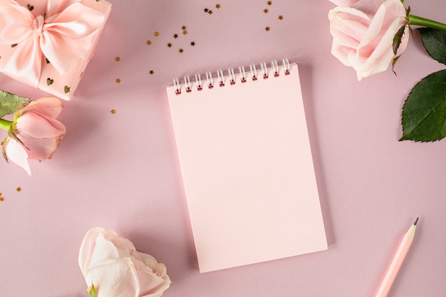 Copy space notepad for your text on a light pink background with pink roses and gift boxes. flat lay. Top view.