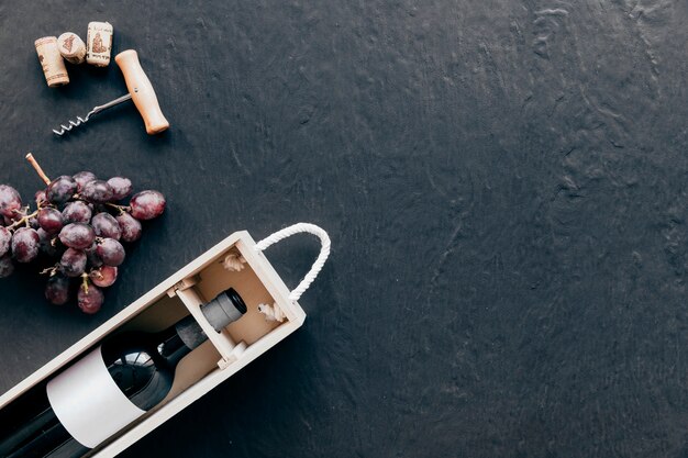 Corkscrew and grape near box with wine