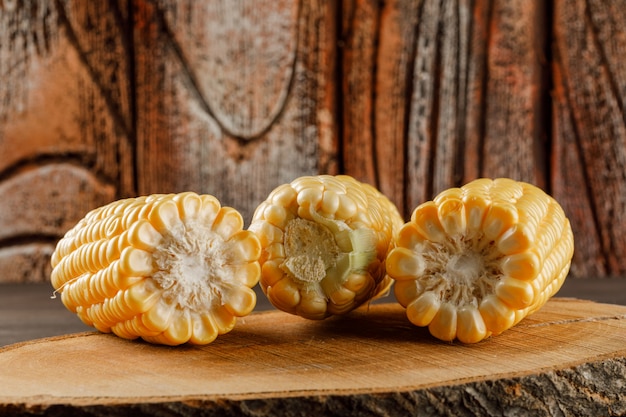 Corn cobs on a wooden piece on brown and stone tile table, side view.