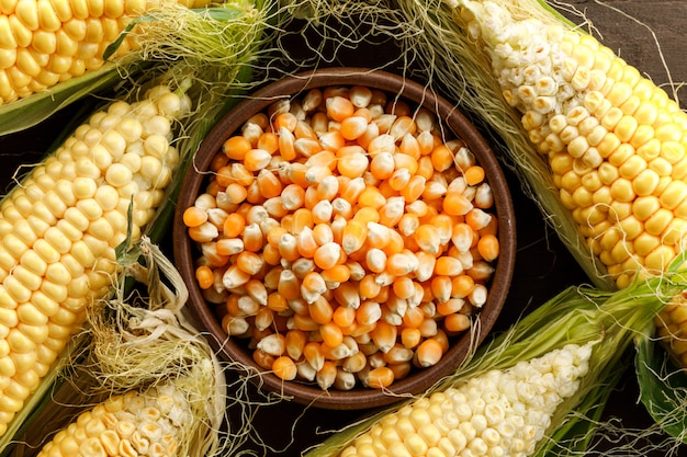 Corn and grains in a clay plate on wooden table, flat lay.