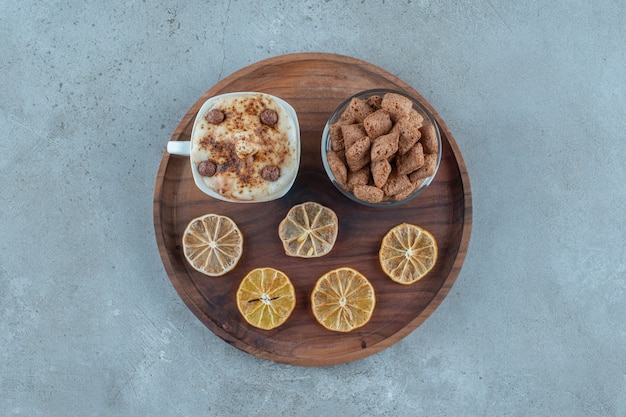 Corn pads on a glass next to lemon slices and a cup of cappuccino on a wooden plate, on the blue background. High quality photo