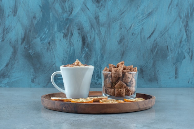 Corn pads on a glass next to lemon slices and a cup of cappuccino on a wooden plate, on the blue table. 