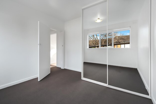 Corner of an empty new room with white walls and a wardrobe with mirror sliding doors